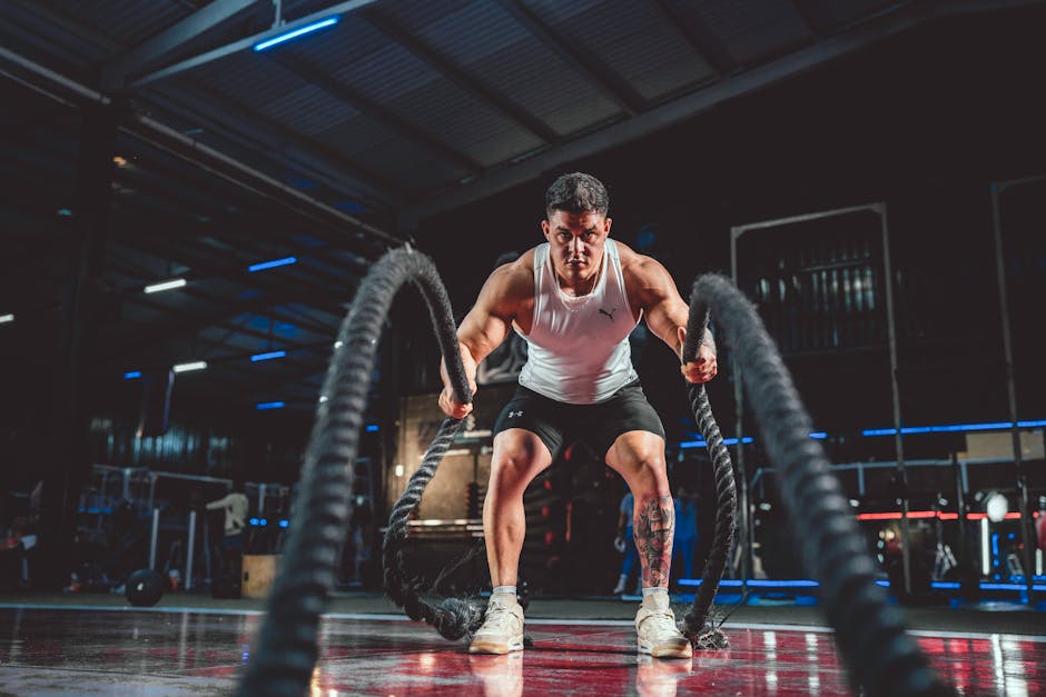 Focused man in white tank top performing battle rope exercise in a modern gym.